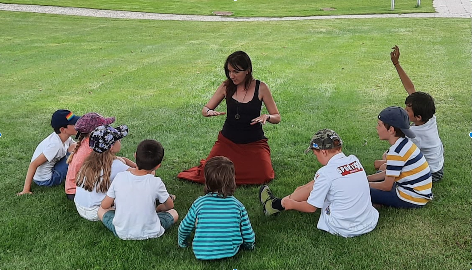 Atelier en plein air : intervenante assise en cercle avec un groupe d enfants